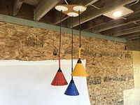 View of all three pendant lights hanging from triangular wood canopy against wooden ceiling and white backdrop