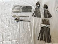 Overview of the full 31-piece cutlery set laid out on white cloth, including knives, forks, spoons, butter knives, and teaspoons with detailed patterned handles.