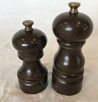 Two wooden Peugeot salt and pepper grinders standing side by side on a cloth surface, showing their size difference and shape.