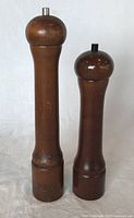 Two wooden Peugeot salt and pepper grinders side by side on a white background, showing full height and wood surface condition.