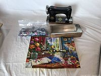 Puzzle pieces in clear plastic bag lying on top of the completed puzzle image showing a vintage sewing room scene. Beside the puzzle is the sewing machine-shaped tin container