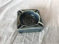 Top view of blue-green glazed square porcelain ashtray with P&O initials inside bowl.