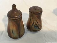 Two ceramic salt and pepper shakers with brown glaze, standing upright.