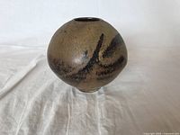 Front angle view showing round shape, matte earthy tones, and dark brown brushstroke design.