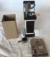 Front view of votive burner with box, pan, pot, and brochure visible