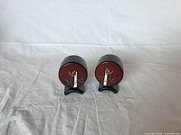 Front view of vintage Japanese salt and pepper shakers with red tops and bamboo design, both shown on black stands against white background.