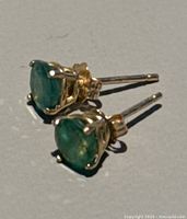 Close-up of both stud earrings showing round green emeralds in yellow gold prong settings