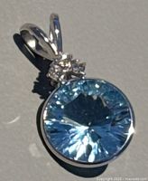 Front view of pendant on grey background showing round blue topaz in bezel setting