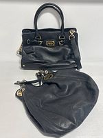 Two Michael Kors black leather handbags shown side by side, both with gold-tone hardware and minor creasing from use.