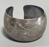 Angled side close-up showing detailed floral and leaf engraving on sterling silver cuff bracelet.