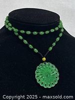 Front view of green jade flower pendant necklace displayed on black bust showing carved flower pendant and beaded necklace.