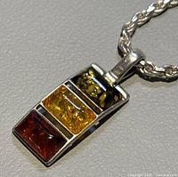 Close-up of pendant showing the three rectangular amber stones in red, yellow and green colors set in polished silver.