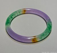 Single round jade bangle shown flat on a light surface highlighting purple, green, and brown color sections.
