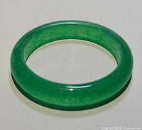 Natural green jade D-shaped bangle bracelet shown laying flat on a light surface, showcasing its color and shape.