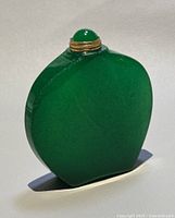 View of the polished natural jade green perfume/snuff bottle standing upright showing the front and stopper with gold-tone collar.