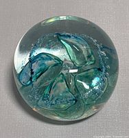 Top view of the art glass paperweight showing internal green and blue abstract shapes with bubbles inside the clear glass sphere.