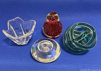 Photo of all four art glass items on a blue background showing bowl and three paperweights.