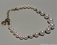 Pearl bracelet laid flat showing graduated pearl sizing and gold-tone spacer beads under direct light.