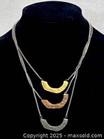 Front view of the three strand necklace displayed on black stand showing three different colored textured metal pendants in gold, copper, and silver tones.