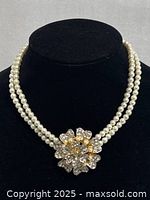 Front view of the double strand pearl necklace displayed on black stand showing the rhinestone flower clasp.