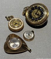 Four vintage pendant watches arranged on a grey textured background showing varying shapes and intricate designs.