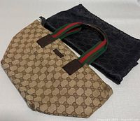 Front view of the Gucci beige canvas handbag with signature GG pattern and green/red fabric handles. Displays full handbag and dust bag beside it.