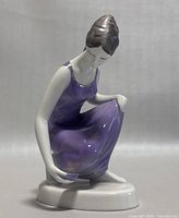 Side view of the hand painted porcelain figurine showing the woman kneeling in a purple dress.