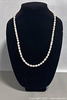 Pearl necklace displayed on black bust showing full length and shape.