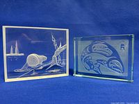 Two rectangular blocks: left is clear Lucite with etched beaver scene, right is blue-tinted etched Native art glass block; both vintage and signed