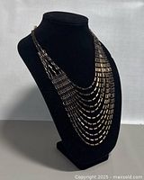Front view of the 17-inch vintage signed statement necklace displayed on a black mannequin. Shows cascading multi-strand design with gold-tone rectangular links and black details.