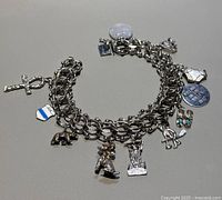 Full view of bracelet arranged in circle showing multiple charms including round discs, figures, and shield