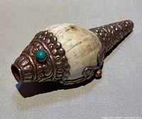 Close-up view of the conch shell front showing metal cap with turquoise stone.