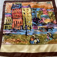 Full flat view of square silk scarf showing colorful old European cityscape painting with cream and chocolate borders.