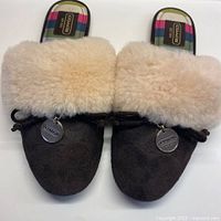 Front view of both slippers showing brown suede exterior, fluffy beige sheepskin cuff and silver Coach metal tags.