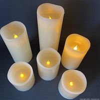 Group of 6 battery operated wax candles shown lit with flickering flame effect on dark background.