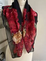 Full view of the black silk chiffon scarf displaying red and yellow roses design draped to show translucency and pattern.