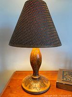 Front view of the lamp on wooden surface showing the woven conical shade and etched wooden base.