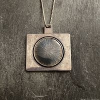 Front view of rectangular sterling silver pendant with circular starburst stone center on silver chain.