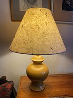 Caramel ceramic lamp illuminated with cream textured shade featuring imbedded wood-like pieces.