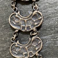 Close-up of two textured crescent-shaped pewter links connected by small round link with visible stamped markings