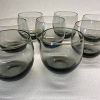 Set of 8 smoky grey lowball glasses grouped together on a white surface, showing their rounded shape and translucent color.