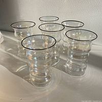 Set of six iridescent glasses with wavy ridges and dark rims arranged on a surface.