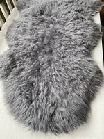 Full view of dark grey sheepskin rug showing its fluffy, thick wool fibers and natural irregular shape.