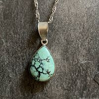 Full view of the sterling silver chain with teardrop turquoise pendant against a textured background