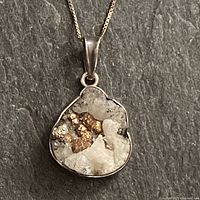 Front view of a quartz geode pendant set in sterling silver, attached to a delicate box chain necklace, shown on a dark textured background.