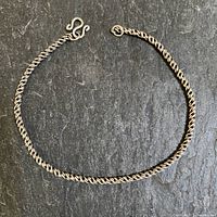 Full length photo of sterling silver twisted rope chain bracelet with hook clasp on a dark textured background.