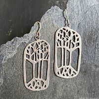 Two sterling silver dangle earrings shown on a stone background, displaying the Tree of Life openwork design.