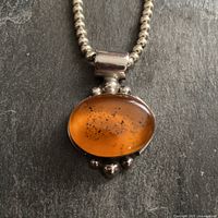 Close-up image of large oval amber cabochon pendant bezel set in sterling silver with silver sphere accents and part of the silver spherical bead necklace.