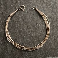 Full view of the multi-strand sterling silver bracelet with cone-shaped ends and spring ring clasp laid flat on dark textured background.