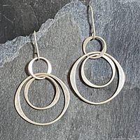 Pair of vintage sterling silver earrings displayed on a dark textured surface showing the three interlocking hoop design and hook fastenings.